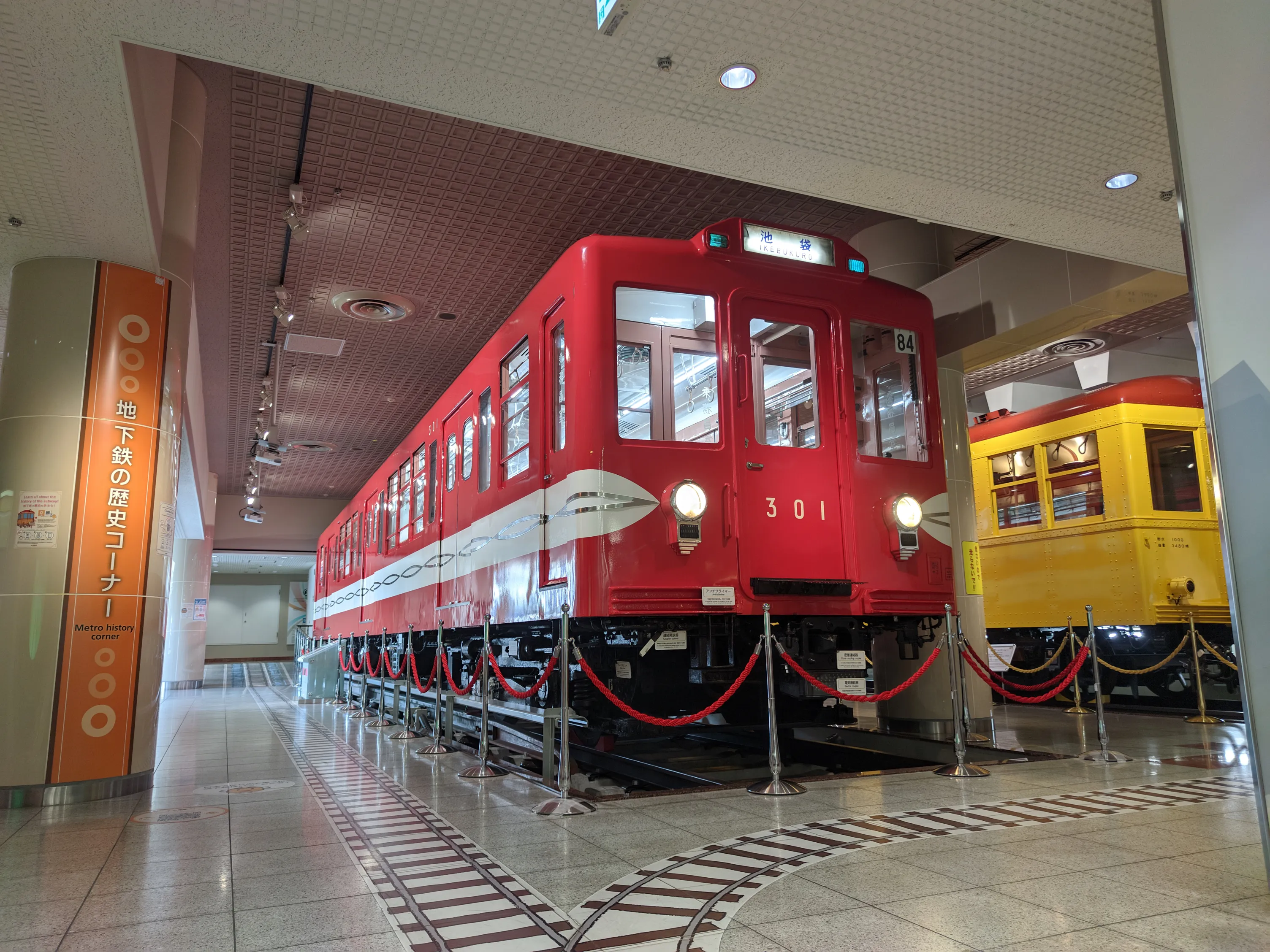 地下鉄博物館の展示コーナー、丸ノ内線の赤い電車を中央に捉え、右には黄色い銀座線の電車もちらっと見える