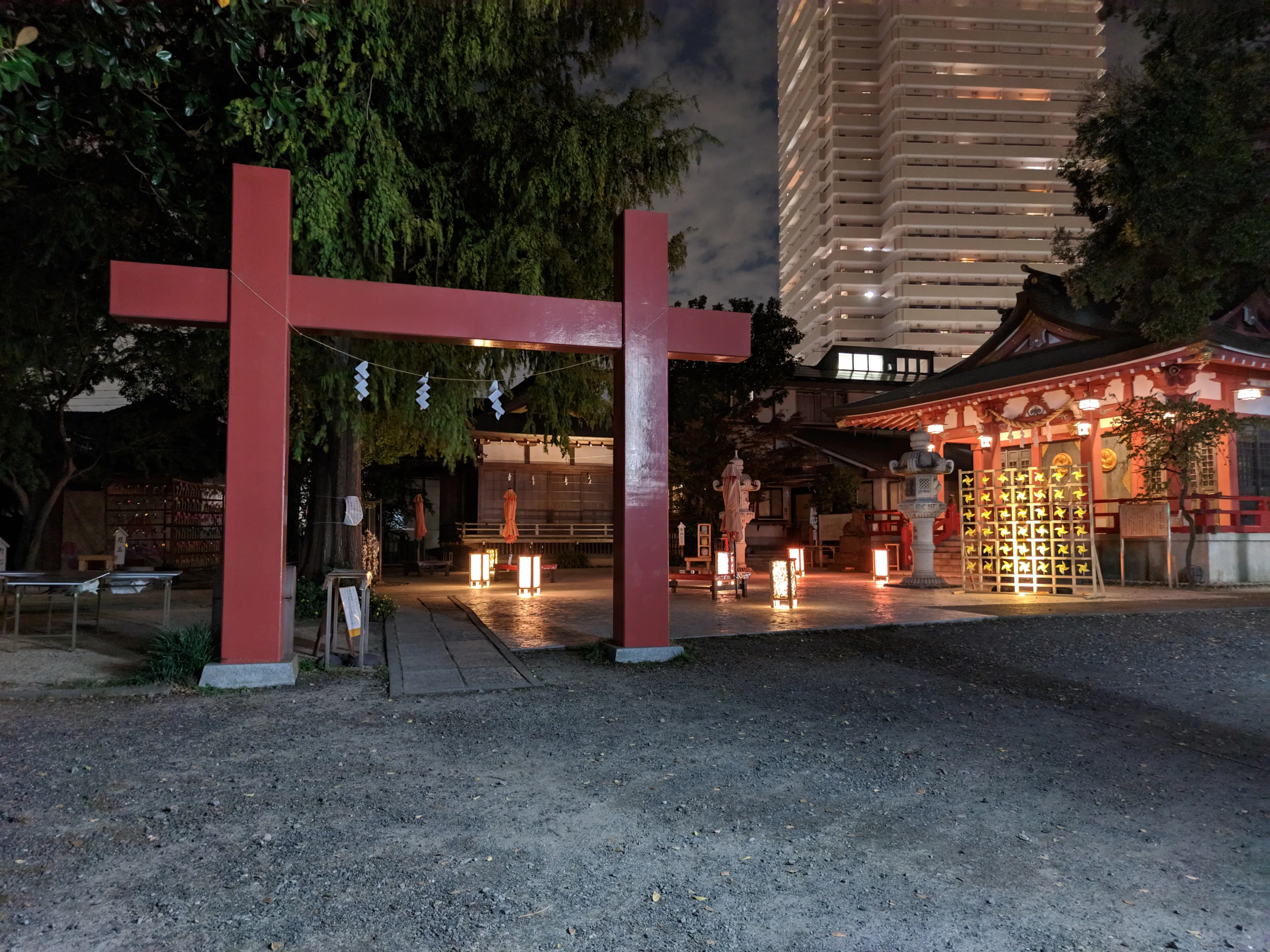 ライトアップされた夜の神社と鳥居、背景にはマンションがそびえ立つ
