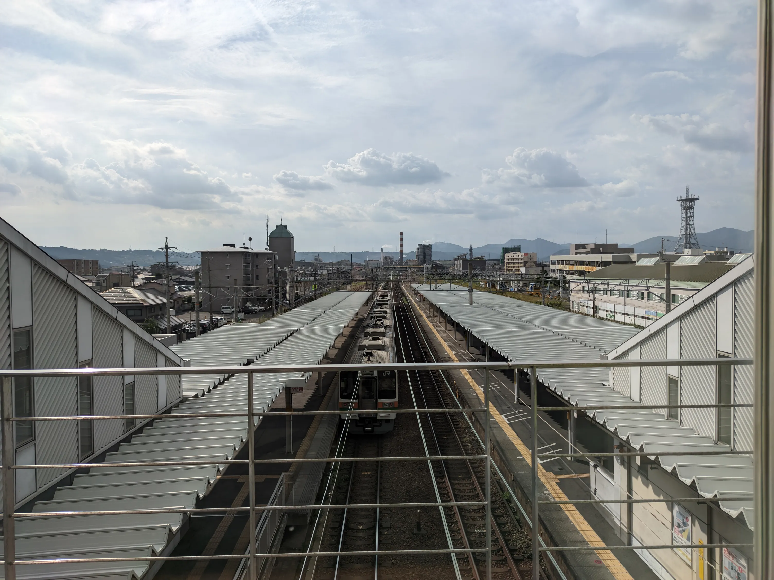 駅の連絡橋の窓から見る水平線、下はプラットフォームと電車、上は青空と雲