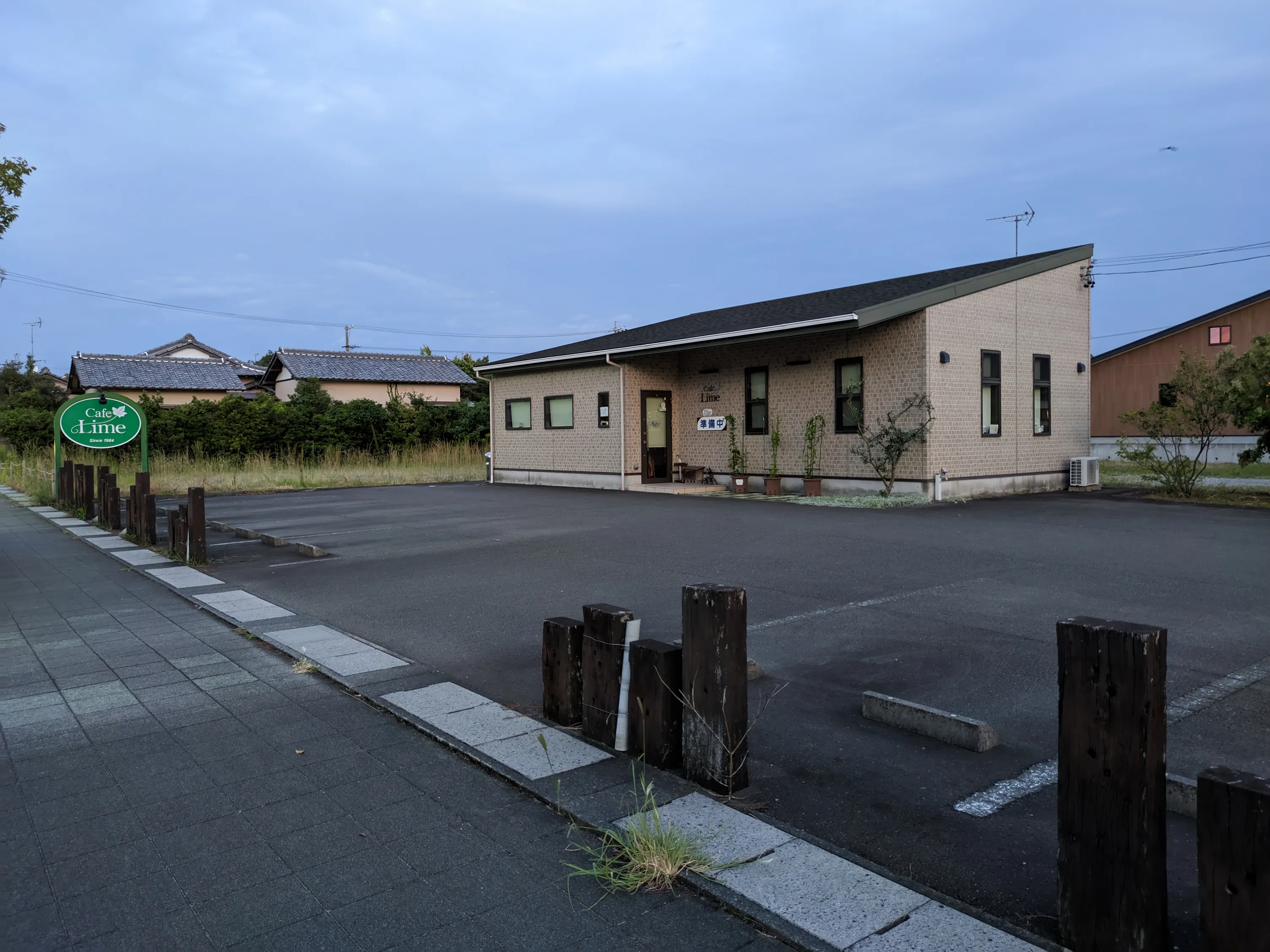 歩道から撮影する喫茶店、曇りの夕暮れ、閉店の札が遠く見えるドアにかかる