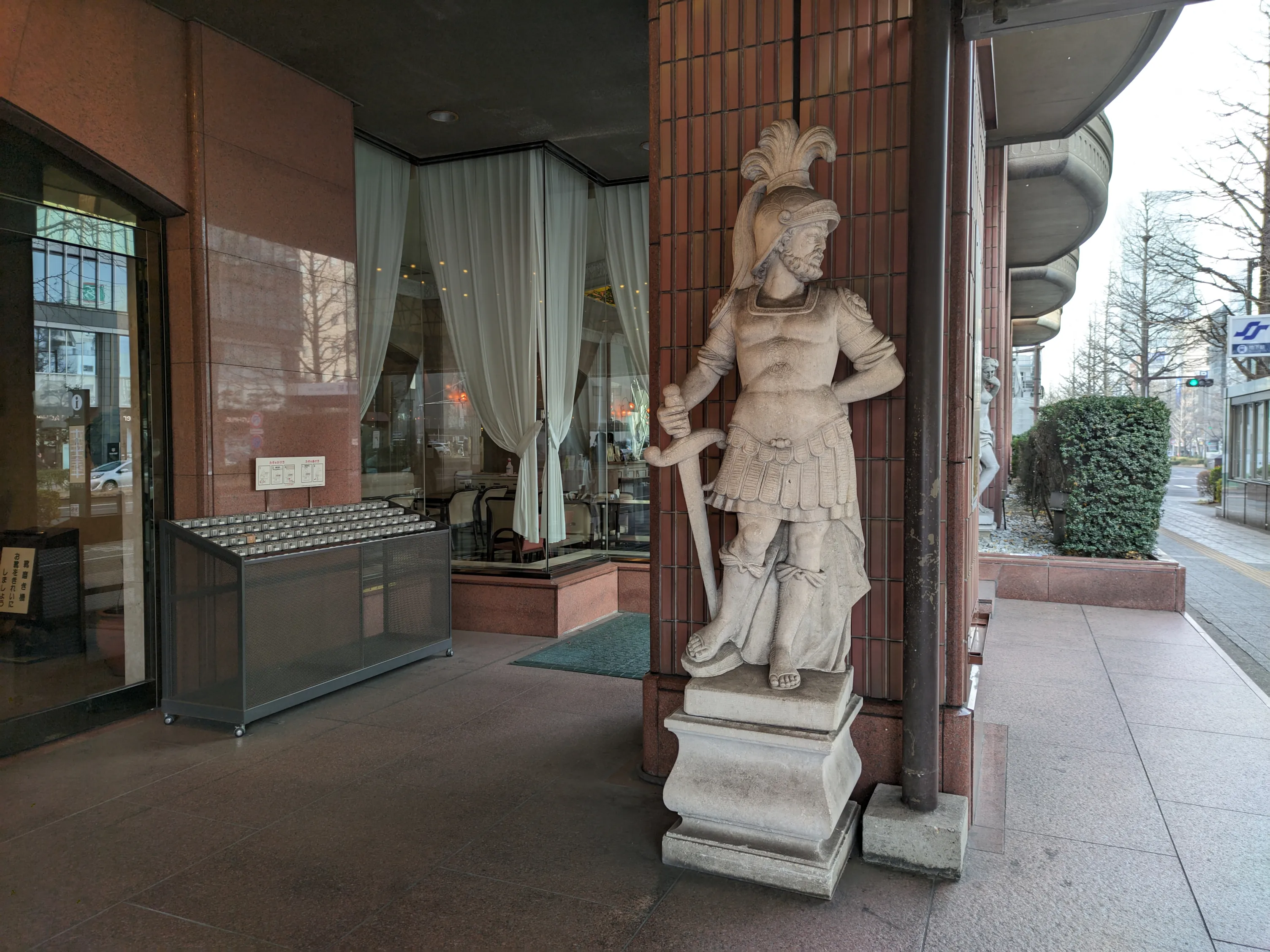 町中にある鎧を着て剣を持った昔の男の石像。現代の町並みを見ているように見える。